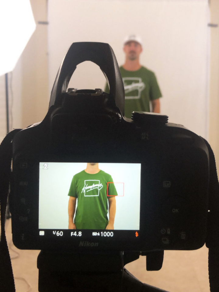 looking through a camera, man wearing an olive green t-shirt with the handsome bogey logo