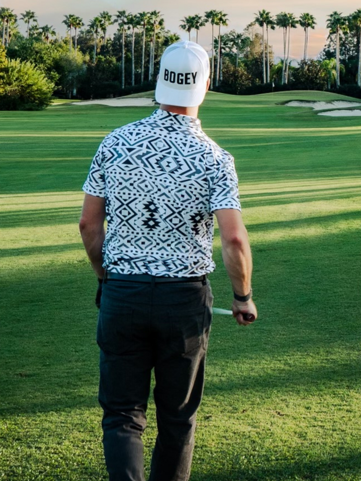 golfer in a black, white, and grey patterned golf polo walking up to hit a golf shot