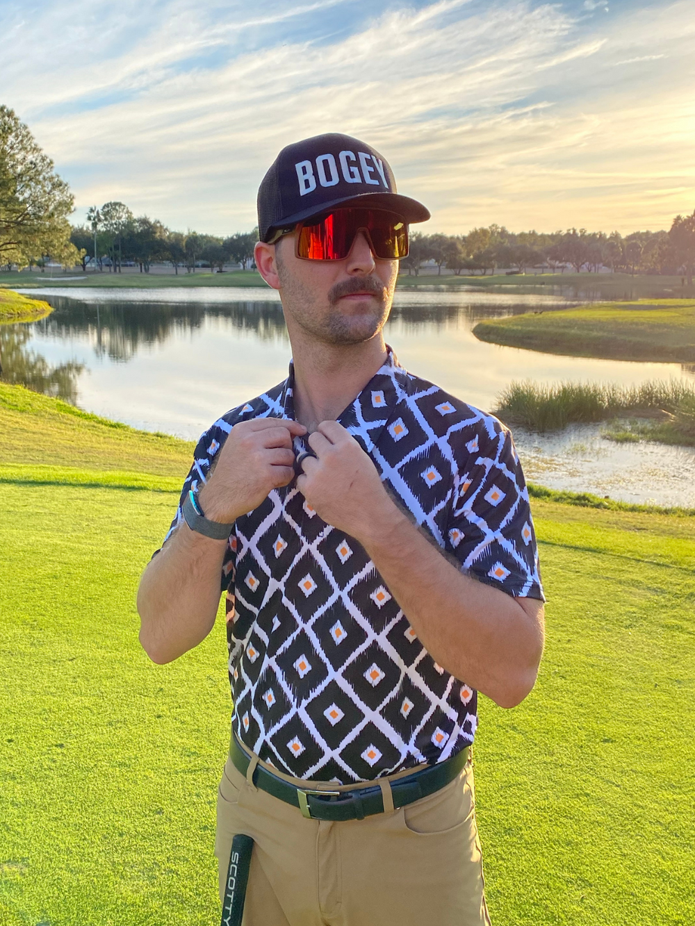 Black, white, and orange diamond patterned golf polo being buttoned in the sunlight, 